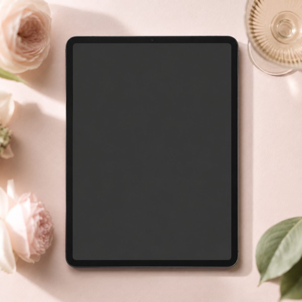 A tablet showing a wedding gallery page, on blush pink with garden roses, a champagne glass and a green leaf