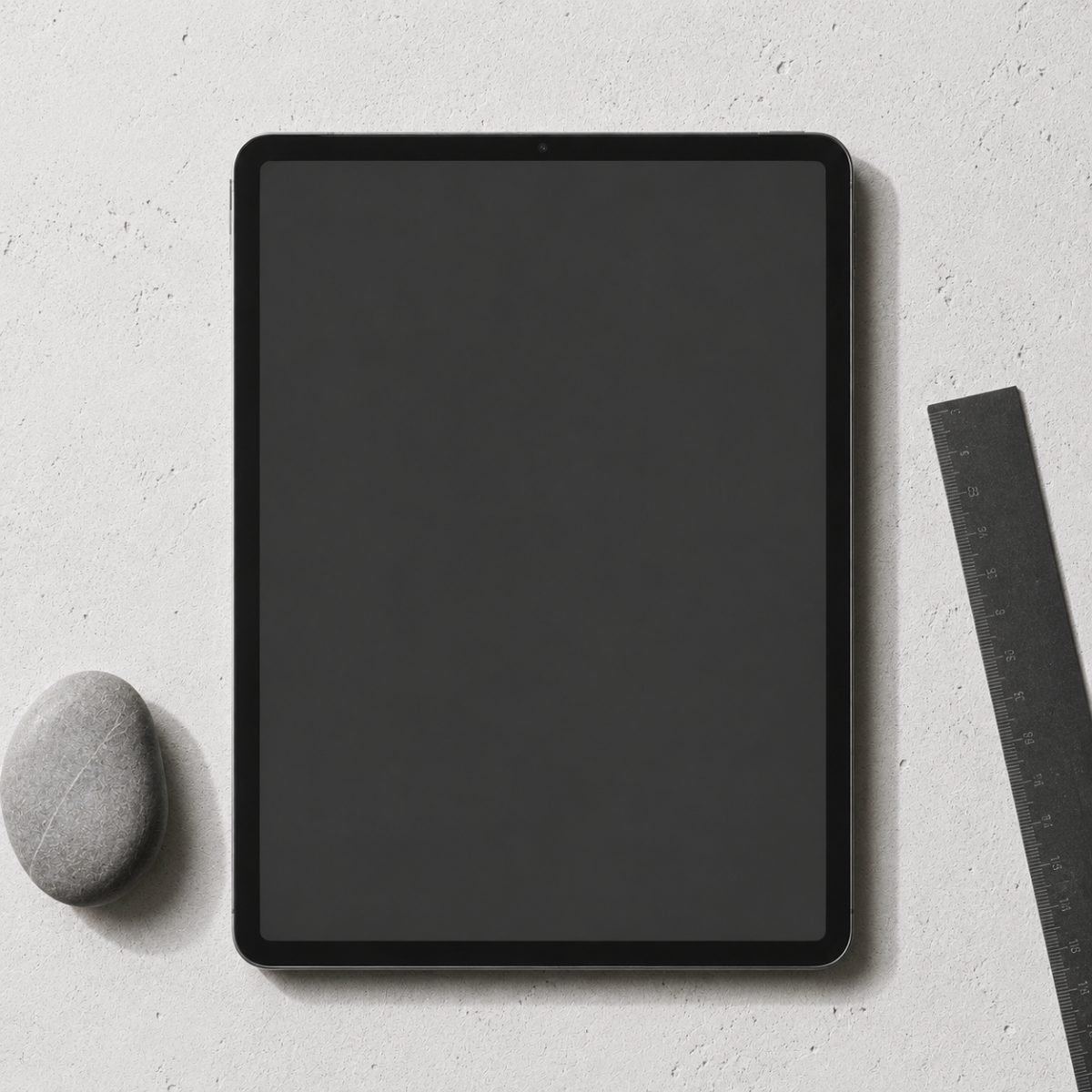 A tablet showing a wedding seating chart, on white concrete with a grey stone and a black steel ruler